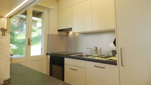 Une cuisine avec des meubles blancs, un plan de travail noir et une fenêtre donnant sur un paysage verdoyant.