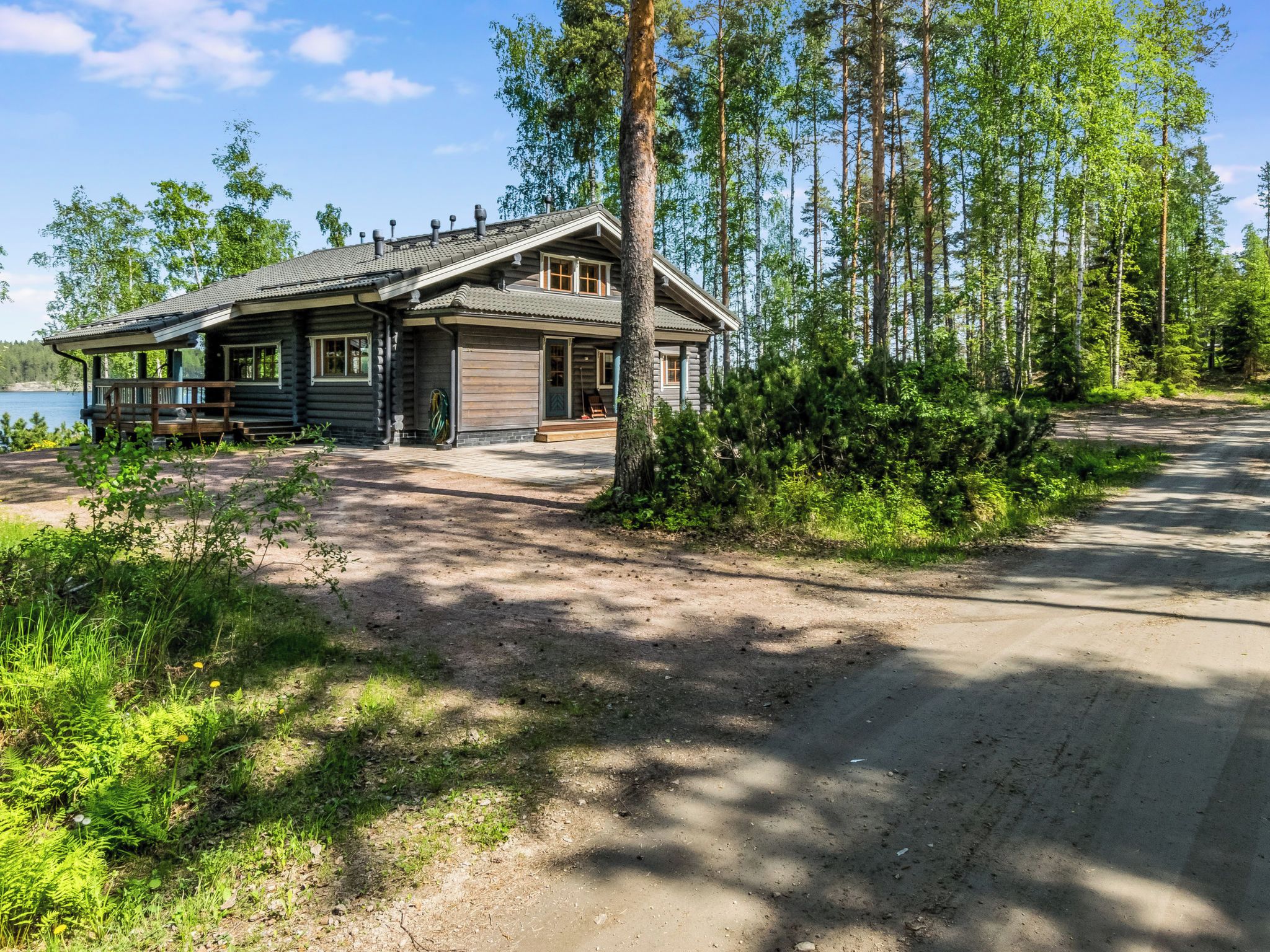Mökki, jossa on kuisti, autotalli ja sorapäällysteinen ajotie, joka johtaa järvelle.