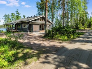 Eine Hütte mit Veranda, Garage und einer unbefestigten Auffahrt, die zu einem See führt.