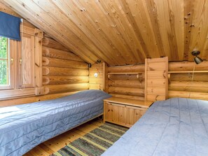 Une cabane avec deux lits, des murs en bois, une fenêtre et un lampadaire au plafond.