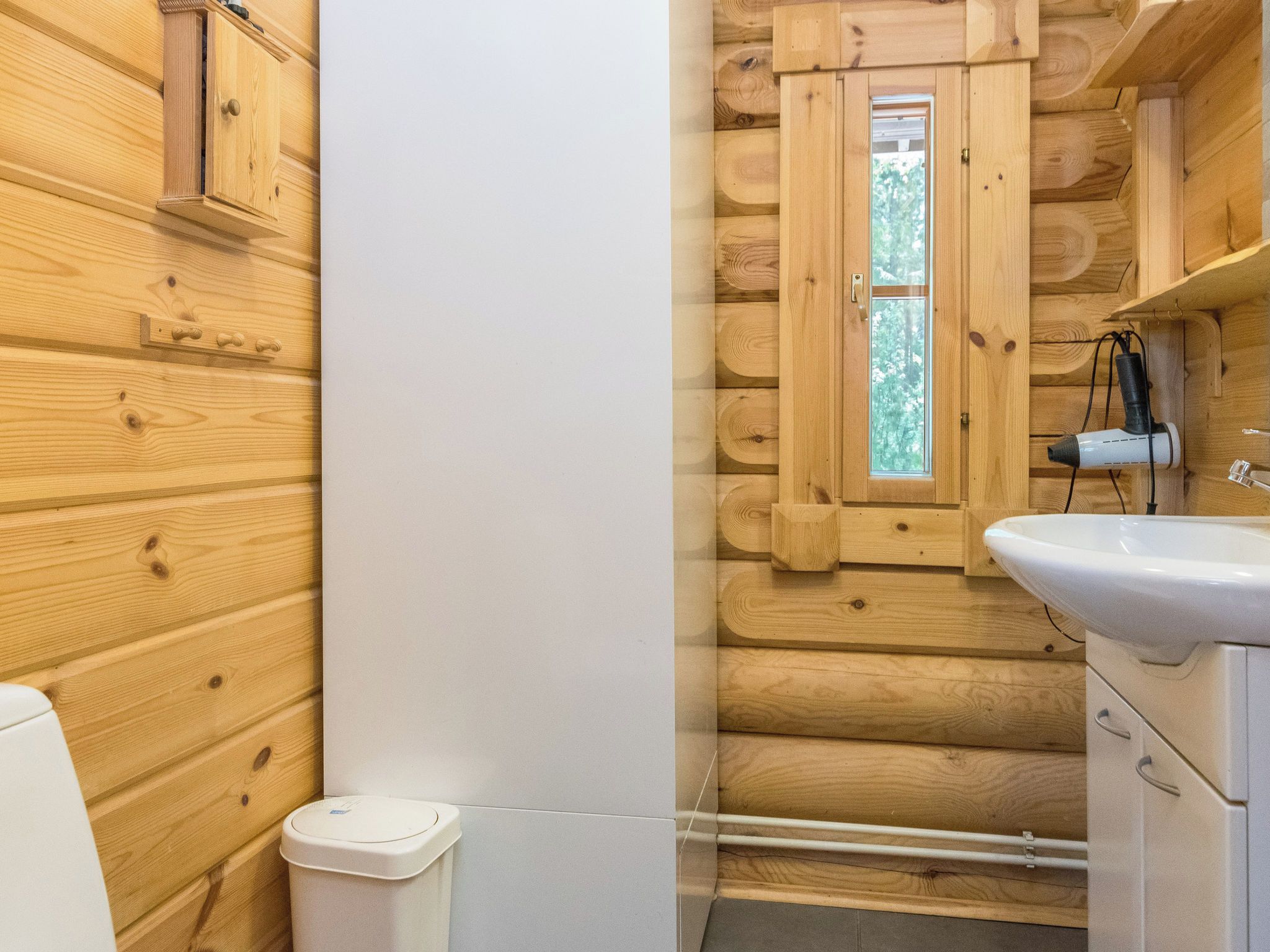Une salle de bain rustique, aménagée dans une cabane en bois, avec une fenêtre, un lavabo et une poubelle.
