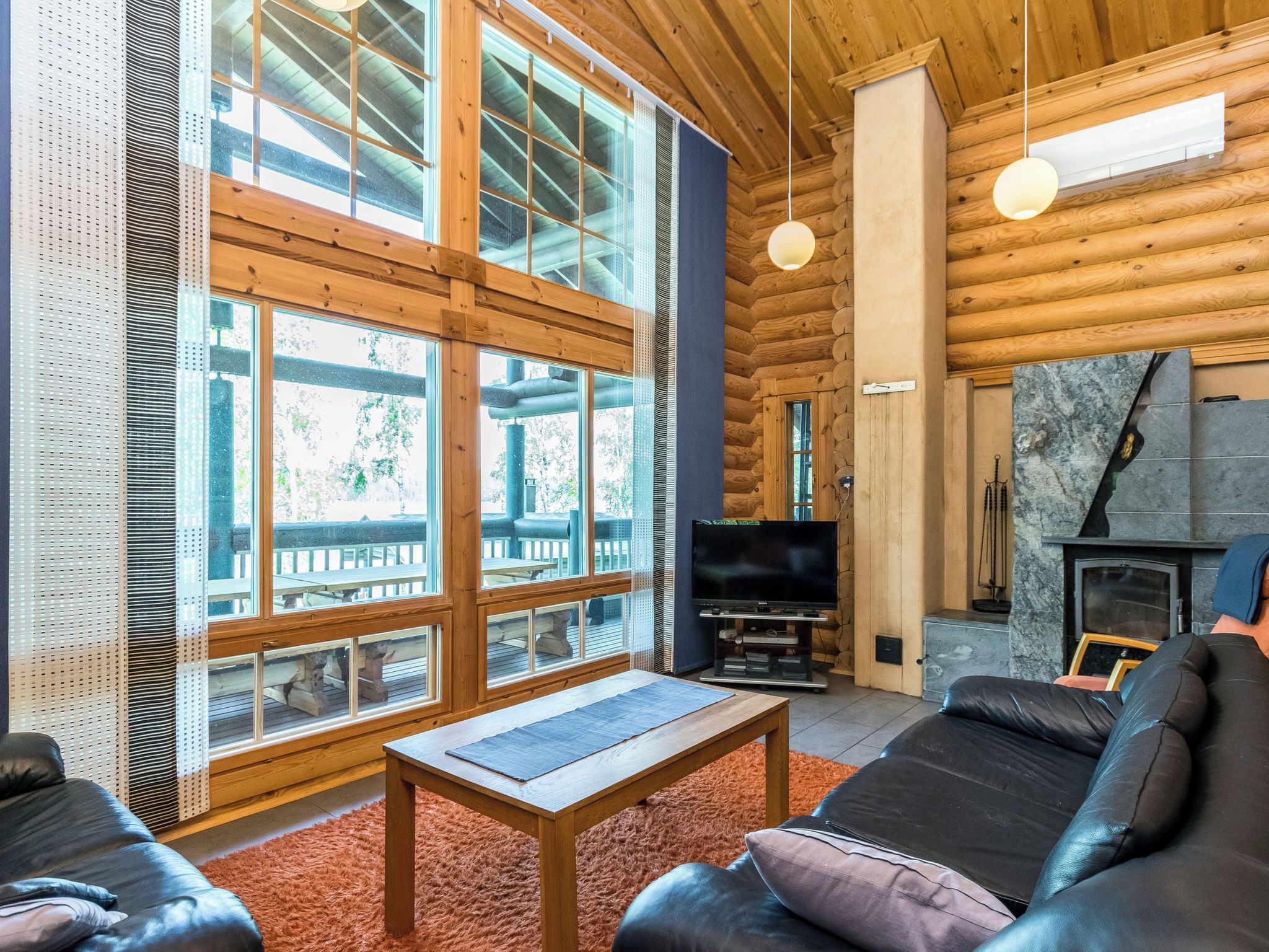 Interior de una cabaña de troncos con chimenea, televisor y zona de estar.