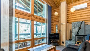 L’intérieur d’une cabane en rondins, avec une cheminée, de grandes fenêtres, un téléviseur et des canapés en cuir.