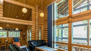 L’intérieur d’une cabane en rondins, avec une grande fenêtre, un canapé, une table et des lampes suspendues.