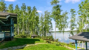 Un chalet au bord du lac, doté d’une terrasse et d’un belvédère, entouré de grands arbres et offrant une vue dégagée sur le lac.