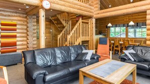L’intérieur d’une cabane en rondins présente un espace de vie avec des canapés en cuir noir, une table basse en bois et un escalier menant à un niveau supérieur.