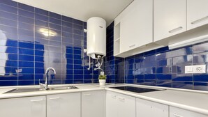 A kitchen with blue tiles, white cabinets, and a water heater. - Platja de Roses by Interhome (Roses)