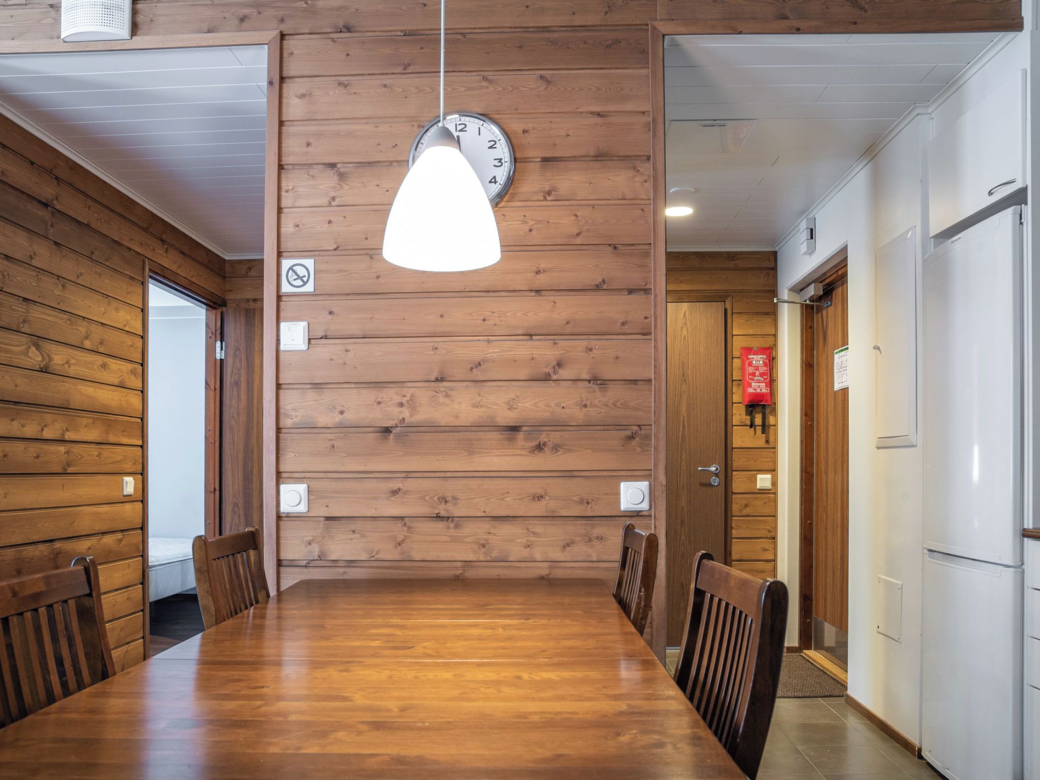 Habitación con paneles de madera, una mesa de comedor, sillas, un reloj y una puerta con un extintor.