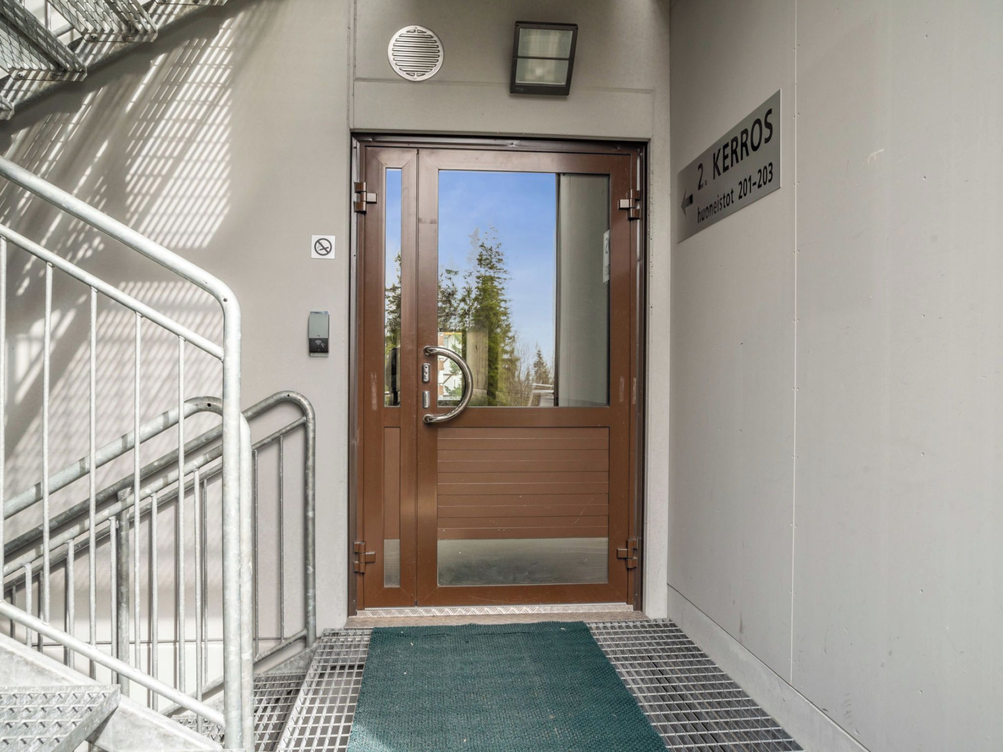 A hotel entrance with a metal staircase, a wooden door with a glass panel, and a green mat at the bottom.