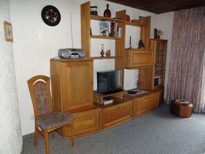 Ein Wohnzimmer mit einer Holz-Unterhaltungseinheit, einem Fernseher, einem Sessel und einer Wanduhr.