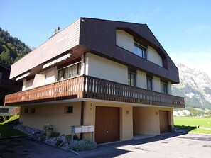 A two-story building with a balcony, a garage, and a mountain backdrop.