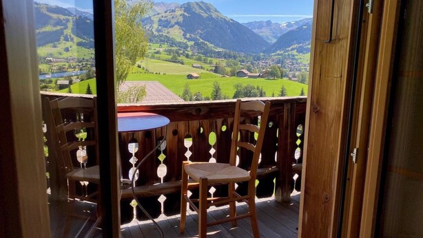 Eine Holzterrasse mit Tisch und zwei Stühlen, mit Blick auf eine Berglandschaft.