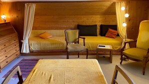 Ein gemütliches Zimmer mit Holzwand, einer Couch, einem Sessel, einem kleinen Tisch und einem Bett.