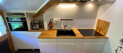A compact kitchen with a built-in oven, a coffee machine, a sink, and a stove.