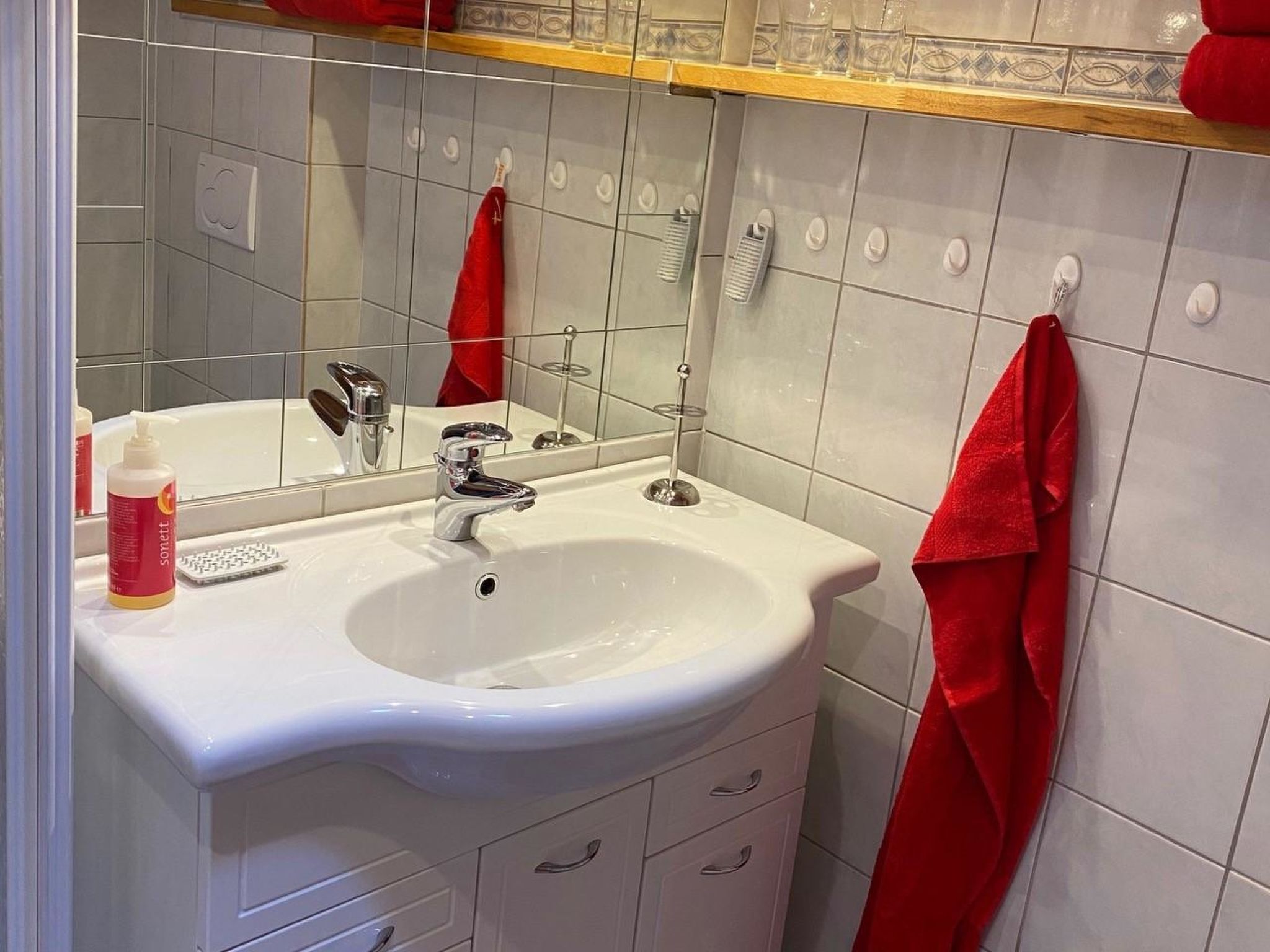 Ein Badezimmer mit einem weißen Waschbecken, einem Spiegel und einem roten Handtuch an der Wand.