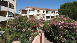 Un immeuble résidentiel à plusieurs étages, doté de balcons, entouré d’une végétation luxuriante et de plantes en fleurs.