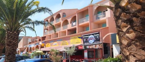Un edificio de varios pisos con balcones, palmeras y un coche azul estacionado frente a él.