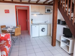 A compact living space with a dining area, kitchenette, and a TV on a stand.