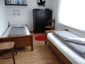 A bedroom with two single beds, a wooden dresser, a chair, and a red rug. - Birkenstrasse 52 Appartement/Fewo 4-Bettwohnung by Interhome (Engelberg)