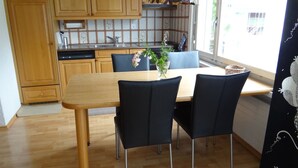 Un comedor con mesa de madera y sillas negras, una cocina con armarios de madera, y una ventana con vistas.