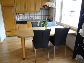 Un'area pranzo con un tavolo di legno e sedie nere, una cucina con mobili in legno e una finestra con vista.