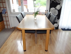 A dining table with four chairs, a vase with flowers, and a view of the outdoors through a window.