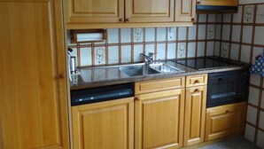 Una cocina con armarios de madera, un lavamanos de acero inoxidable, un lavavajillas y un microondas negro.