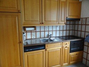 Una cucina con mobili in legno, un lavandino in acciaio inossidabile, una lavastoviglie e un forno a microonde nero.