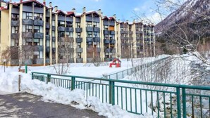 A multi-story building with balconies, a snow-covered ground, and a mountainous backdrop. - Grand Roc by Interhome (Argentière)