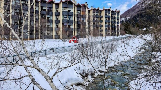 A multi-story building with balconies, a river in the foreground, and a mountainous backdrop. - Grand Roc by Interhome (Argentière)