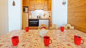 A cozy kitchen with wooden cabinets, a microwave, oven, and dishwasher. There are four red mugs on a table with a white teapot.