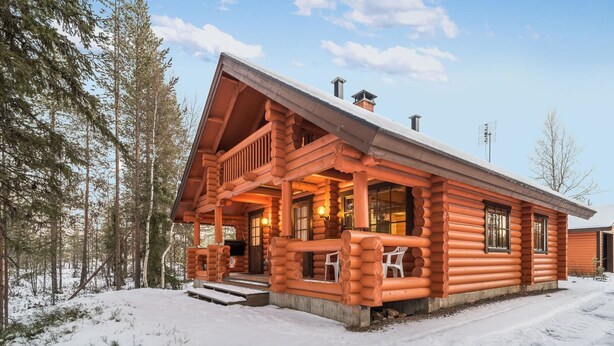 Eine Blockhütte mit Veranda, Treppen zum Eingang und einer schneebedeckten Landschaft.