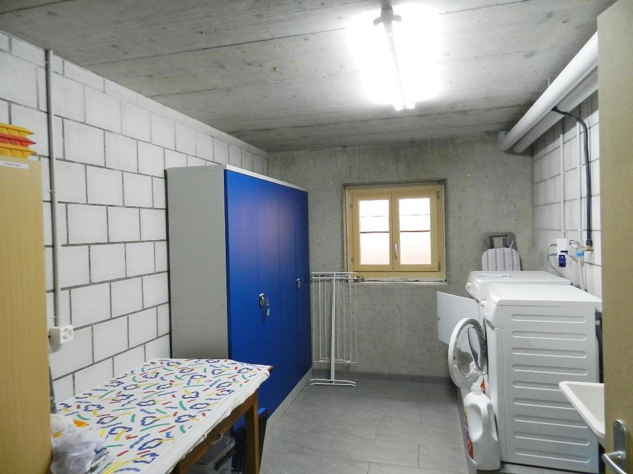 Ein kleines, zweckmäßiges Badezimmer mit einem blauen Schrank, einem Fenster und einer Waschmaschine.