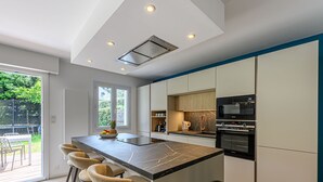A modern kitchen with a central island, bar stools, a microwave, oven, and a sink. - Les Marines by Interhome (Carnac)