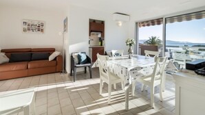 Uma sala de estar moderna com um sofá marrom, uma mesa de jantar com cadeiras brancas e uma área de cozinha.