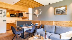 Een moderne woonkamer met een grijze bank, een houten eettafel gedekt voor vier personen, en een keuken op de achtergrond.