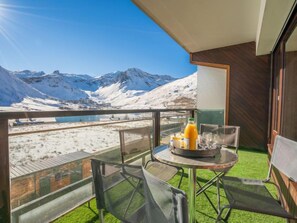 A balcony with a table set for two, a bottle of orange juice, and a glass. The balcony overlooks a snowy mountain landscape. - Les Cimes (Le Lac) by Interhome (Tignes)