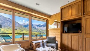 Een modern vakantiehuis met grote ramen en een prachtig uitzicht op de bergen, een gezellige zithoek met een tafel gedekt voor twee personen, en houten kasten.