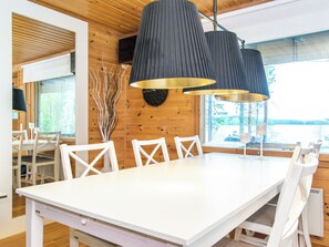 A modern dining area with a white table and chairs, a black ceiling light fixture, and a window with a view of trees.