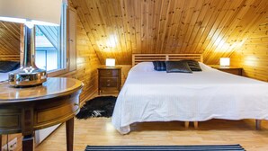 A cozy attic bedroom with a wooden sloped ceiling, a large bed with white bedding, two bedside lamps, a wooden nightstand, and a mirror. - Tipuniemi by Interhome (Hämeenlinna)