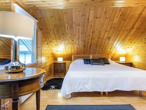 Une chambre avec un plafond en pente, un lit avec une literie blanche, deux tables de chevet avec des lampes, une commode en bois et un tapis sur le sol.