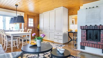 Un saló d'estar acollidor amb una llar de foc, sostre de fusta i zona de dinar amb caires i taula.