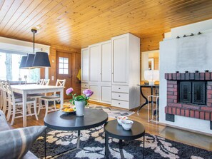A cozy living room with a fireplace, wooden ceiling, and a dining area with chairs and a table. - Tipuniemi by Interhome (Hämeenlinna)