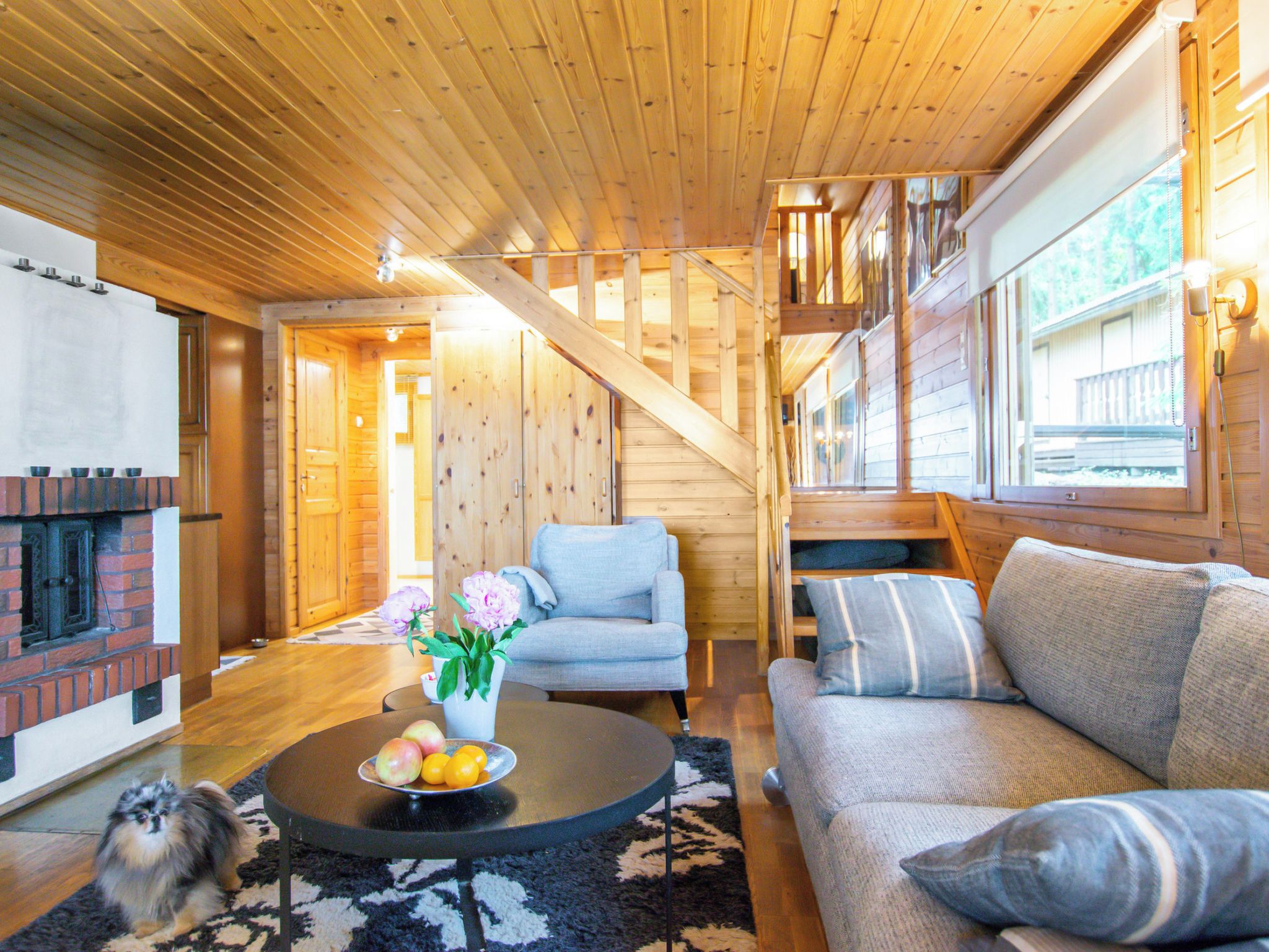 L’intérieur d’un chalet accueillant, avec une cheminée, des murs en bois, un canapé, un fauteuil et une table à manger agrémentée de fruits.