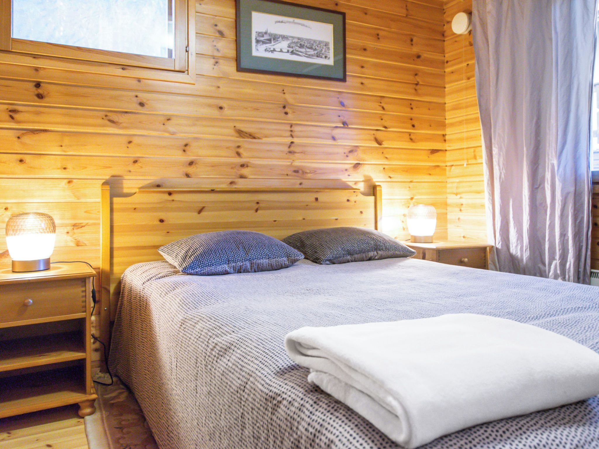 Une chambre à coucher dans un chalet en bois, avec un lit, deux lampes de chevet, une table de chevet et un tableau encadré au mur.
