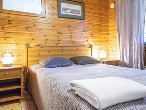 Un dormitorio de cabaña de madera con una cama, dos lámparas de noche, una mesita de noche y un cuadro en la pared.
