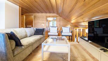 L’intérieur d’un chalet confortable, avec une cheminée, un canapé, une table basse en verre et un téléviseur.