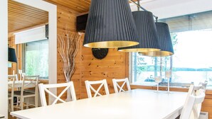 A modern dining area with a white table and chairs, black pendant lights, and a view of the outdoors. - Tipuniemi by Interhome (Hämeenlinna)