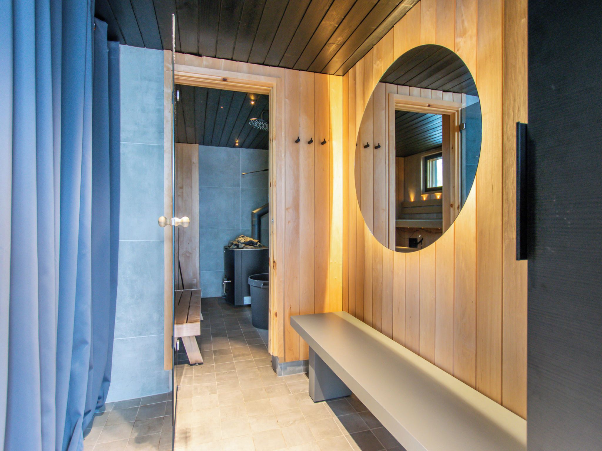 Un couloir avec un banc en bois, un miroir rond et une porte donnant sur une salle de bain.