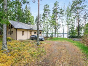 A cabin with a gravel driveway, surrounded by tall pine trees and a body of water in the background. - Tipuniemi by Interhome (Hämeenlinna)